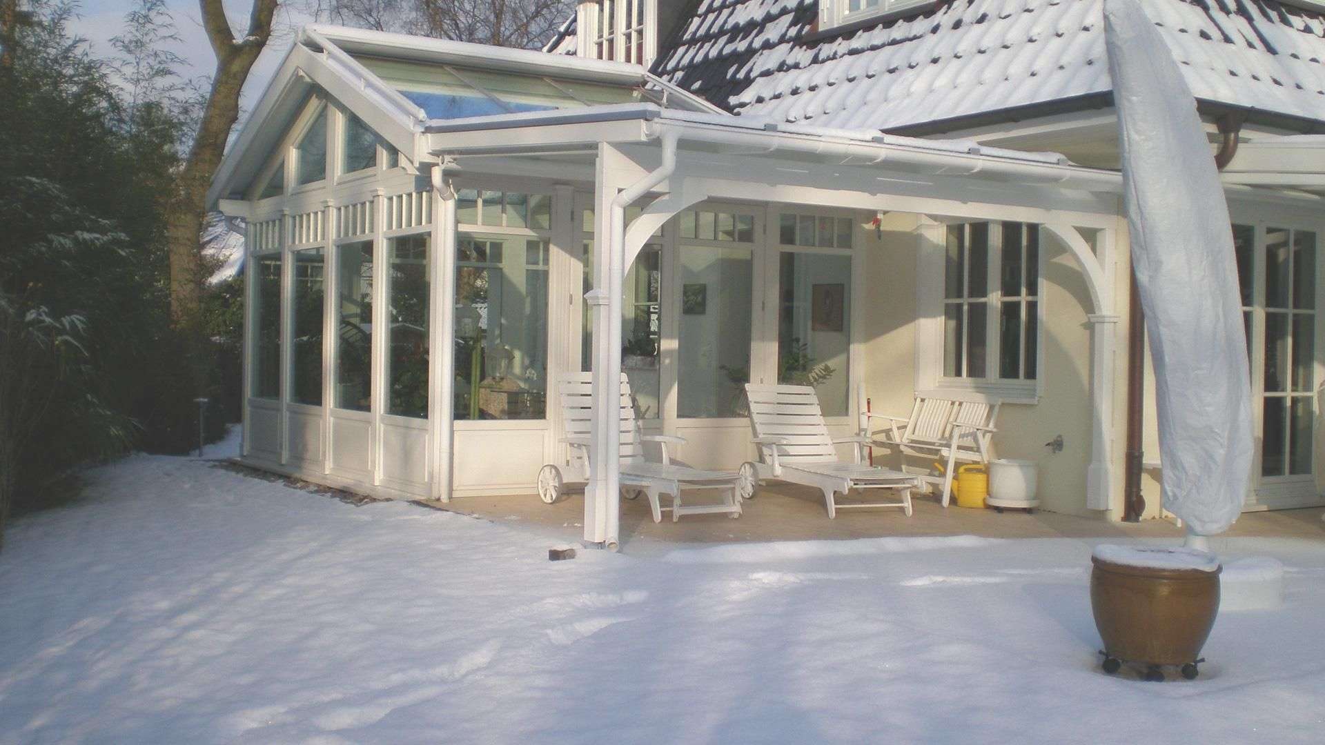 Wintergarten mit Flügeldach an einem Wohnhaus mit schneebedecktem Garten