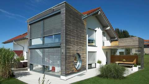 modernes Haus mit Sonnenschutzrollos vor den bodentiefen Fenstern