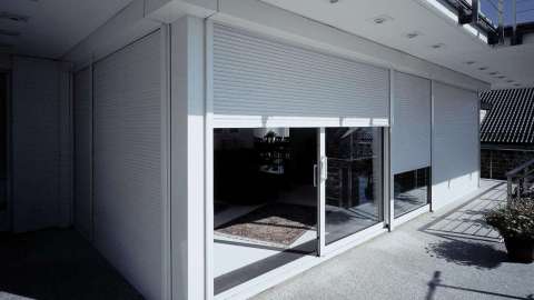 Blick auf Hausecke mit Glasfront und halb geschlossenen Rollläden