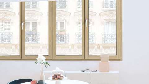 vier Holz-Aluminiumfenster in einer weißen Wand mit Tisch im Vordergrund