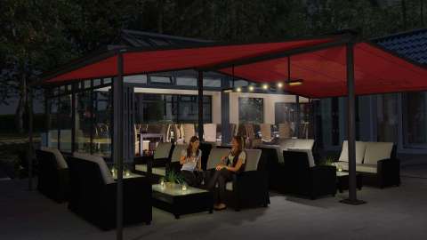 Lounge mit Sitzmöbeln überdacht mit roter Syncra Markise bei Nacht