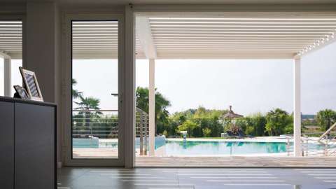 Wohnzimmer mit angrenzender Pratic VISION HI-Pergola mit Blick auf einen Pool