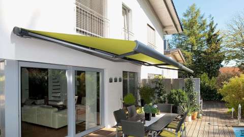 grüne Markise über einer Terrasse mit Esstisch an einem weißen Haus