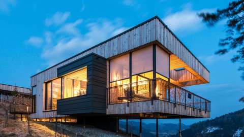 modernes Flachdachhaus aus Holz mit Textilscreens bei Dämmerung, drinnen beleuchtet