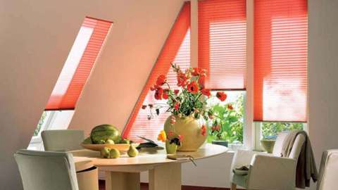 rote Plissees vor Dachfenstern und schrägen Fenstern eines Essbereichs