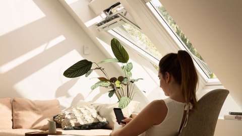  VELUX INTEGRA® Dachfenster unter dem eine Frau am Handy sitzt