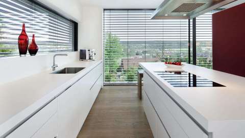 Blick in eine moderne Küche mit großen Fenstern, die mit Raffstores verdunkelt sind