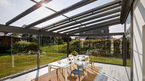 Innenansicht eines Glashauses mit Esstisch mit Blick in den grünen Garten