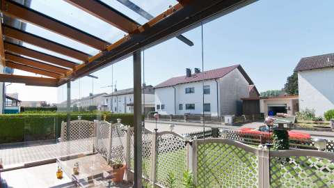 Innenansicht eines Glashaus mit Zaun davor und Blick auf eine Wohnsiedlung