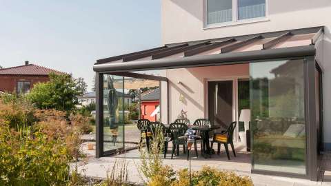 Glashaus mit Gartenmöbeln an einem Wohnhaus