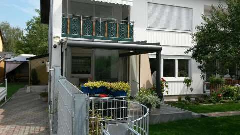 Glashaus an einem weißen Reihenendhaus mit Balkon und Zaun um den Garten