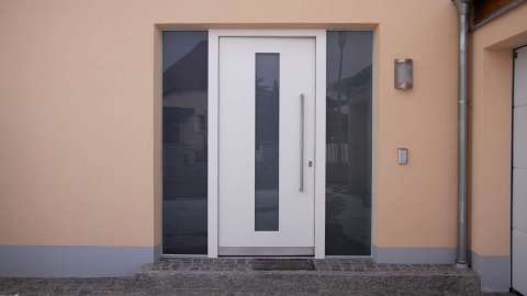 weiße Haustür mit Glaselementen rechts und links in aprikot-farbender Fassade