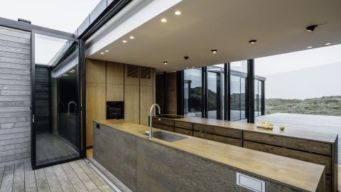 Herzstück des Hauses ist die Küche: Sie ist räumliches Verbindungsglied zwischen Schlaf- und Wohnbereich und kann mithilfe der hochwärmegedämmten Glas-Faltwände Highline auf zwei Seiten vollständig geöffnet werden.  Bildnachweis: Malik Pahlmann