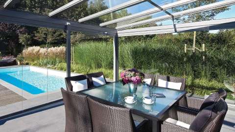 Innenansicht eines Glashaus mit Esstisch im Inneren und Blick auf den Garten mit Pool