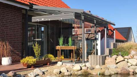 Glashaus an einem Wohnhaus mit Teich im Garten