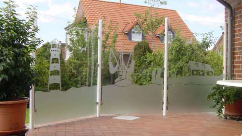 Windwand aus Glas um eine Terrasse vor einem Wohnhaus