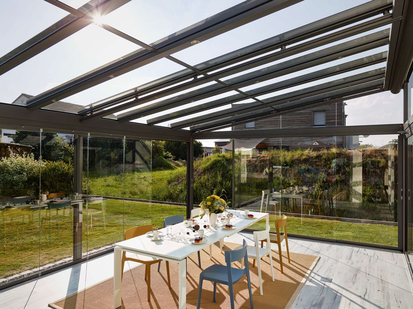 Innenansicht eines Glashauses mit Esstisch mit Blick in den grünen Garten