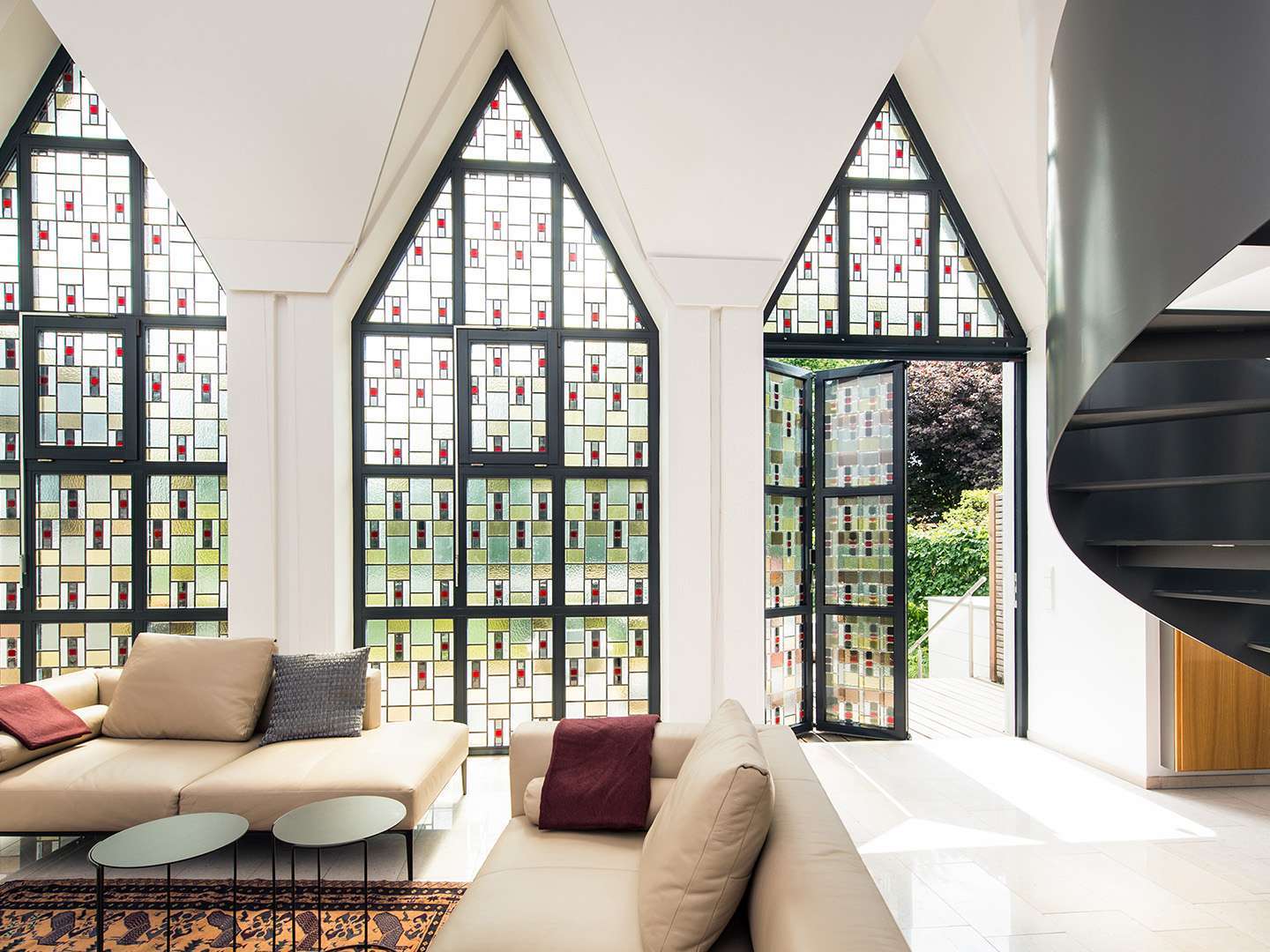 Innenansicht eines Wohnzimmers mit dreieckigen Buntglasfenstern und geöffneter Glas-Faltwand
