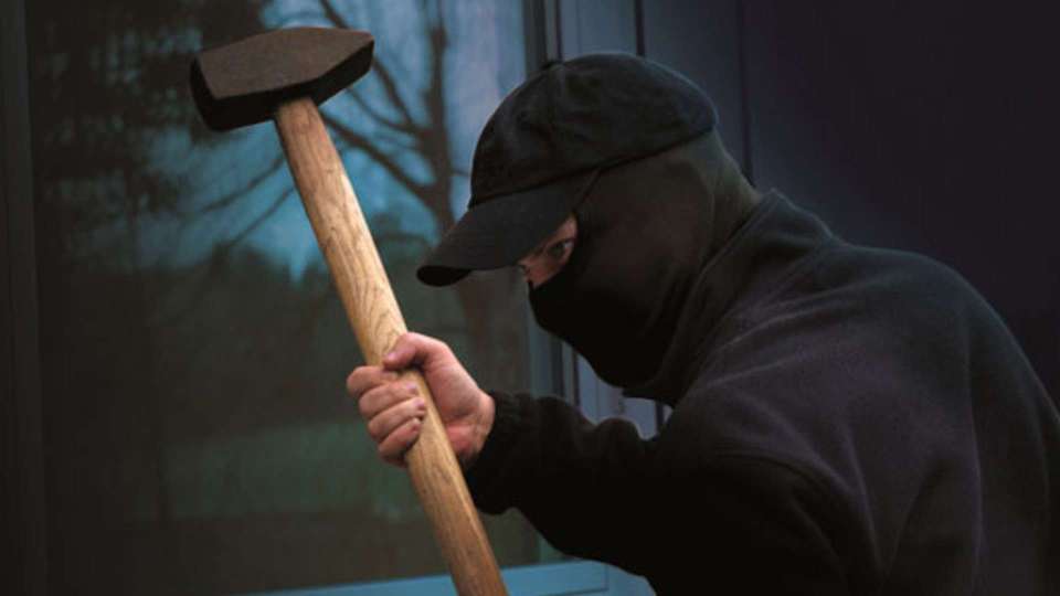 Einbrecher mit einem Hammer vor einem Fenster mit Sicherheitsglas