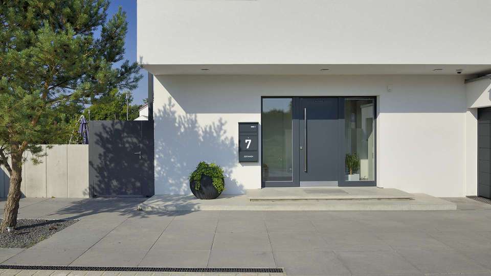 graue Haustür mit Glaselementen auf beiden Seiten in einem weißen Haus